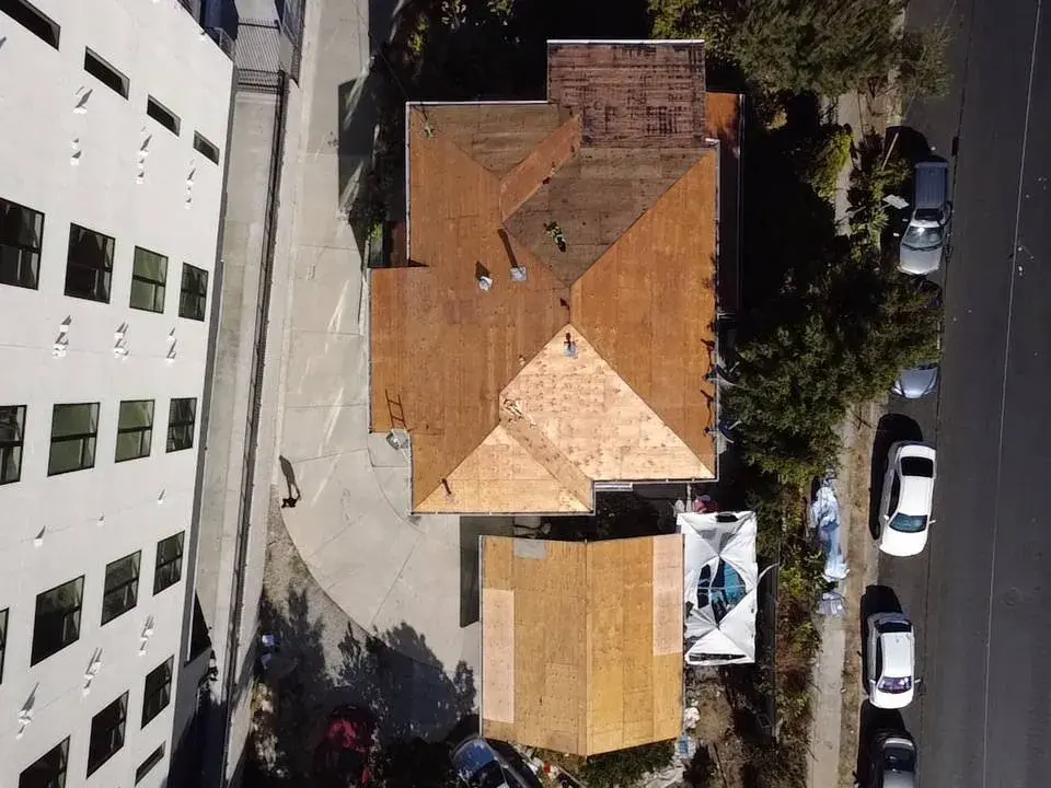 New plywood sheathing on a hip roof next to an apartment building