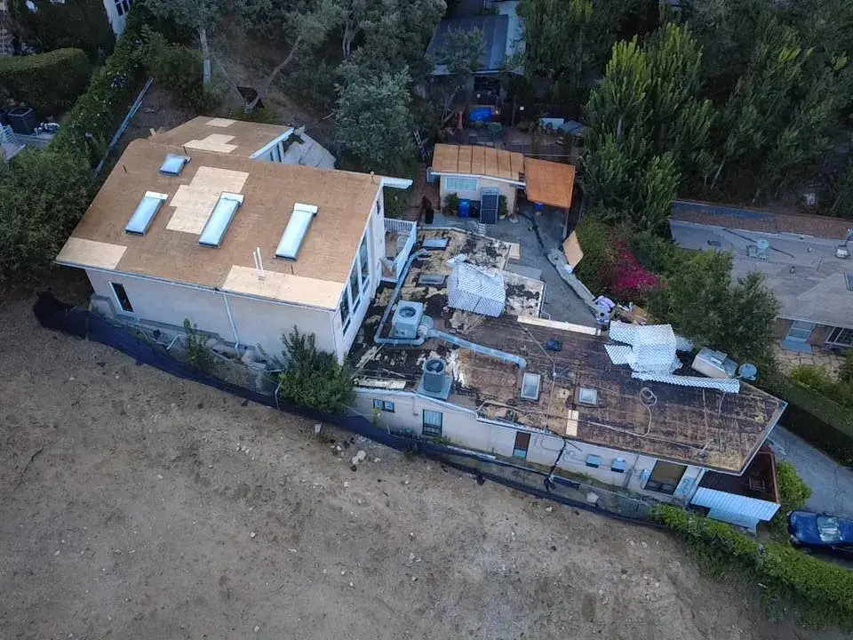 Aerial view of a roof tear-off in progress on a hillside home