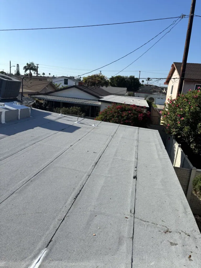 Flat roof covered with a new gray membrane, power lines and neighboring houses beyond