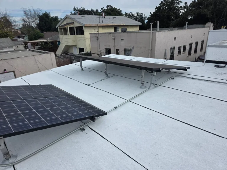 Flat roof with a white coated surface and solar panels on raised racks with conduit crossing the roof