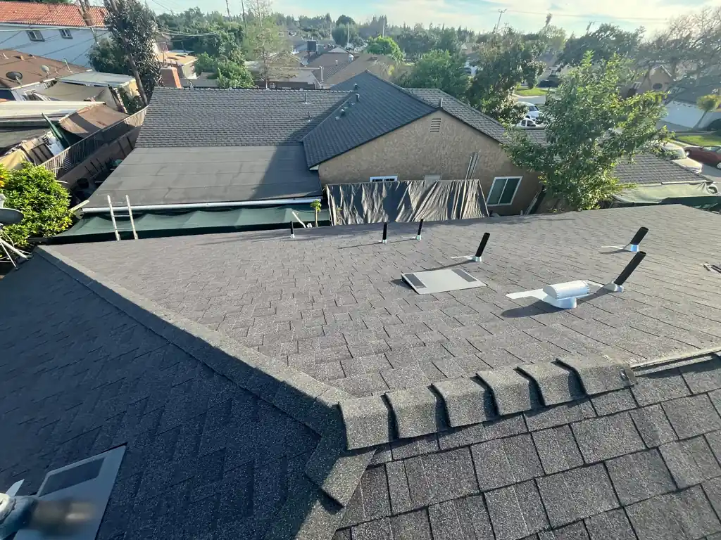 New gray shingle roof with a capped ridge, roof vents and pipe vents, neighboring houses behind