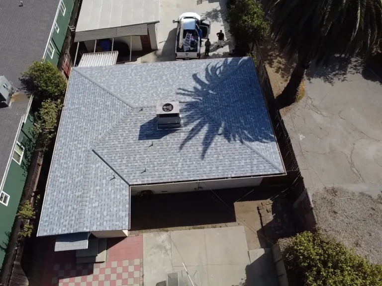 Aerial view of a finished light gray shingle roof with a rooftop air unit and a work truck with a ladder nearby