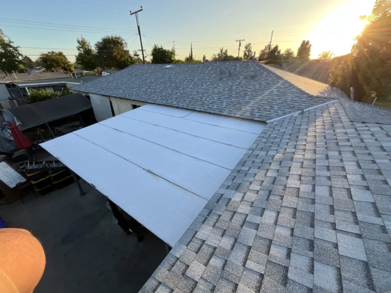 New gray shingles on a roof with a white underlayment section over the patio at sunset