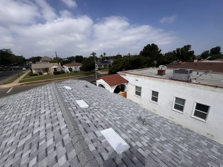 New light gray shingle roof with several white vents above a white stucco home with a clay tile accent